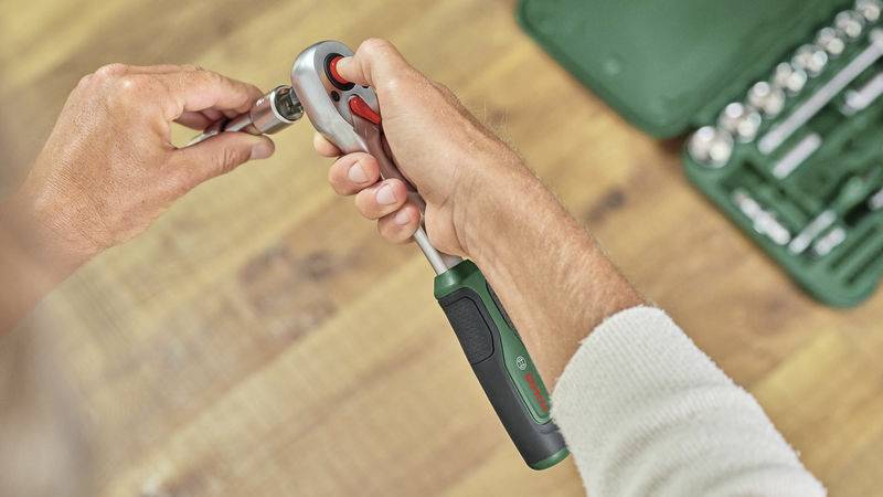 A person is holding a spanner and securing a socket. A toolbox can be seen in the background.