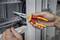 A person is holding a red and yellow combination pliers and bending a cable in front of an open electrical cabinet.