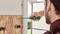 A person is tightening a screw into a wooden board with a screwdriver. The hand is supporting the board, with a window in the background.