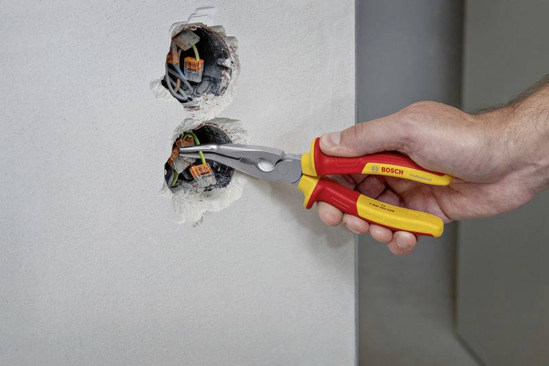 A hand is using red and yellow wire cutting tools to connect cables in an electrical socket.