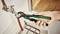 A hand is using an adjustable spanner to tighten a pipe beneath a sink. The spanner has a green handle.
