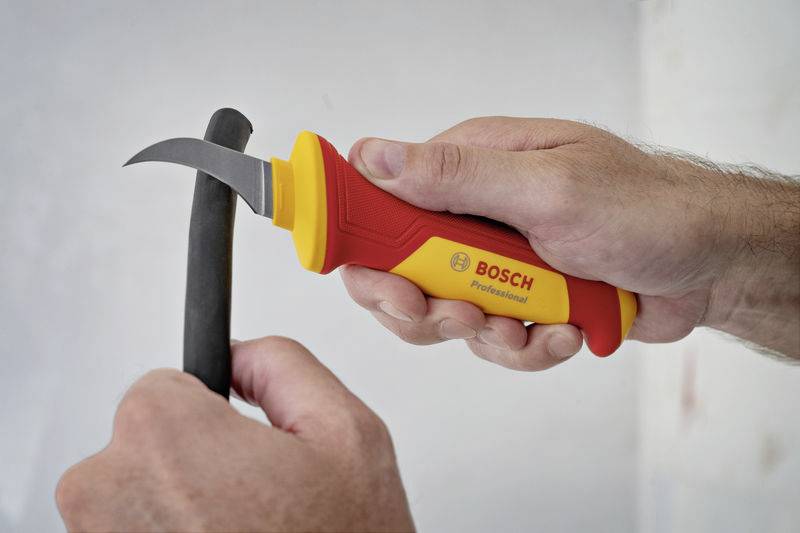 A person is using a yellow Bosch cable knife with a red handle to precisely strip a cable.