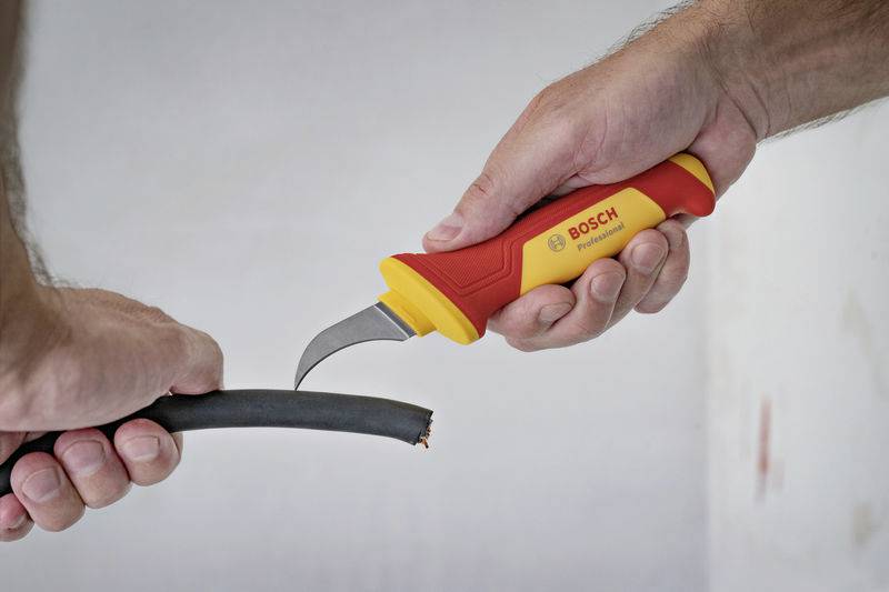 A person is cutting a cable with a special knife that has a red and yellow handle, labelled with 'BOSCH'.