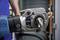 A hydraulic pipe wrench is being used on a pipe. It is being held by a person wearing a blue boiler suit.