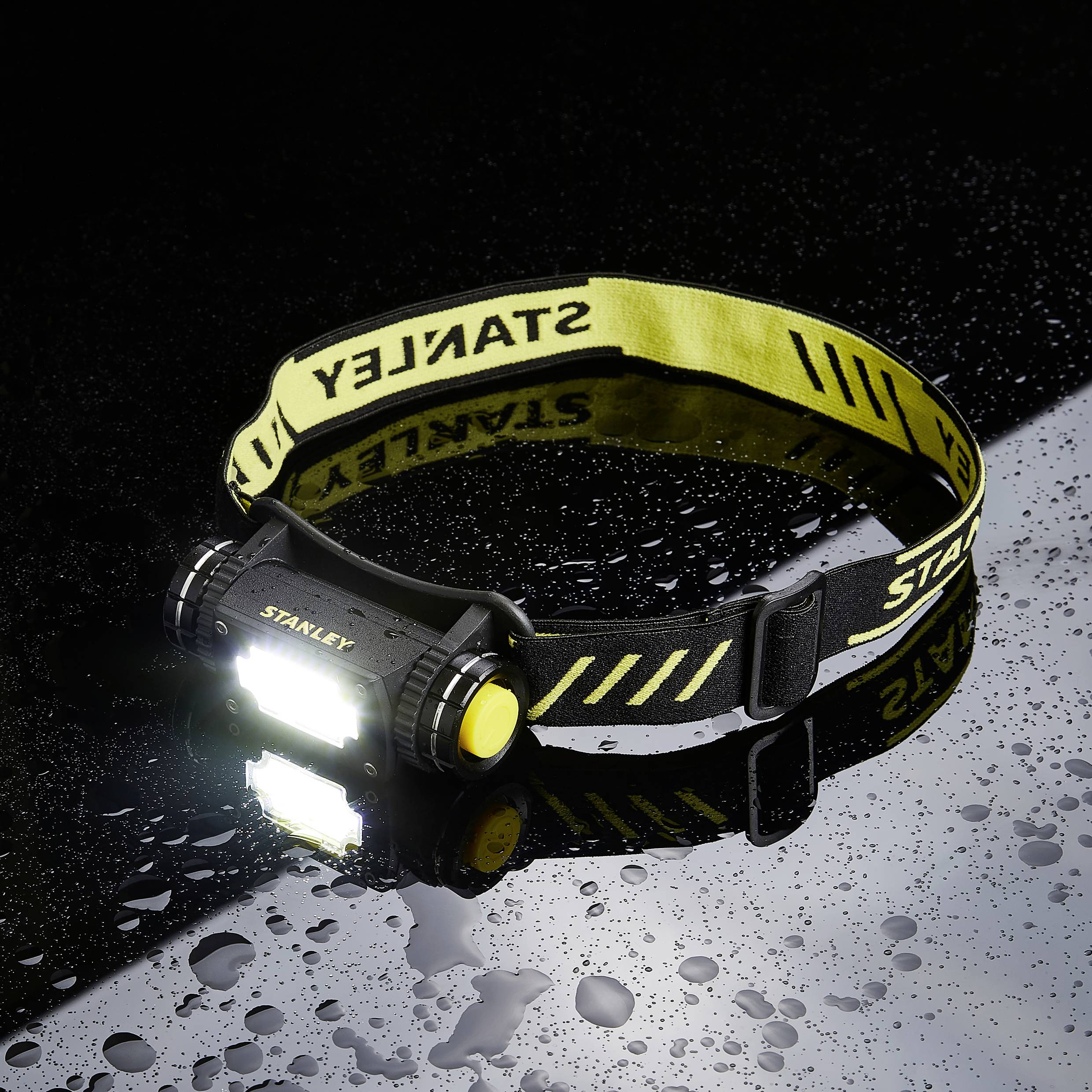 A waterproof LED headband with a yellow band lies on a wet, dark surface, glowing brightly and slightly reflecting.