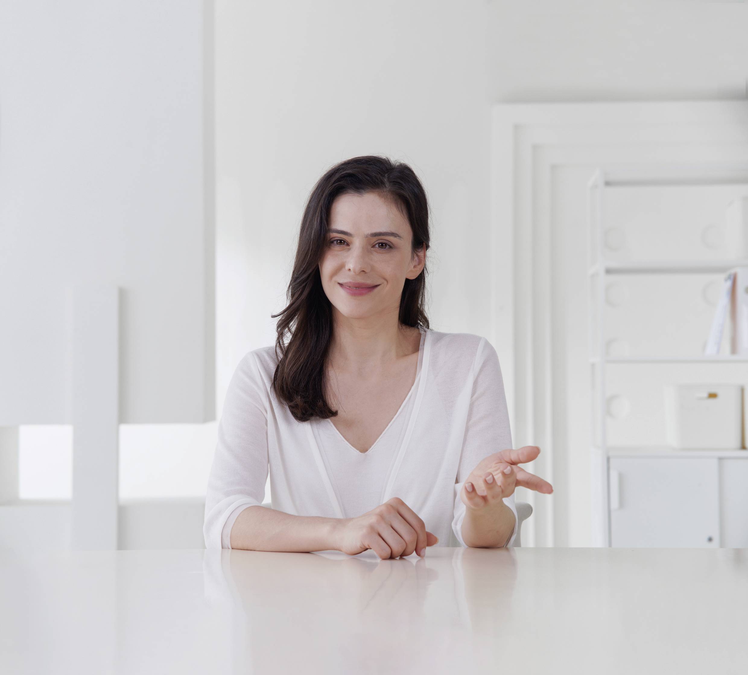 A person is sitting smiling at a table in a bright room.