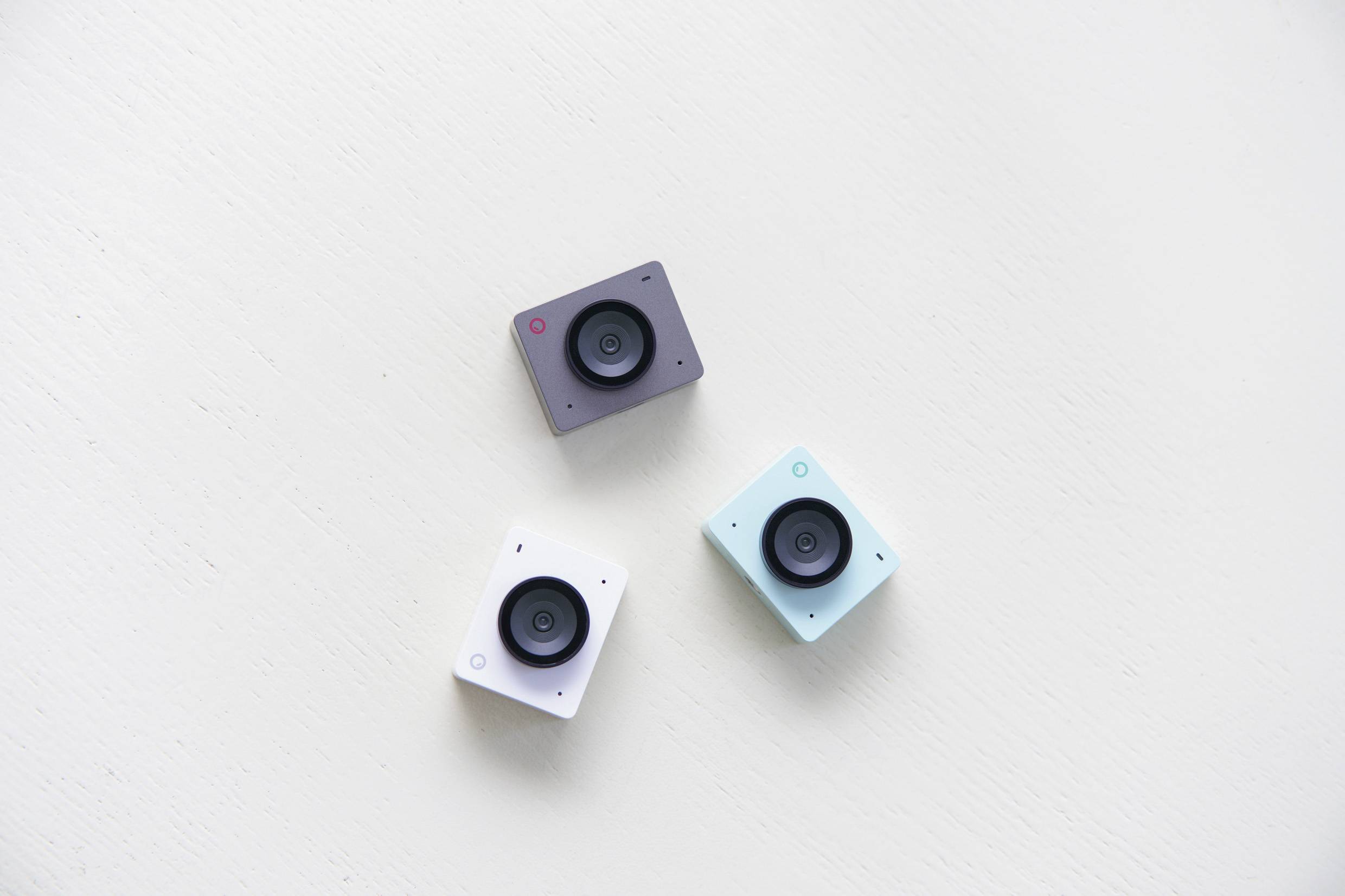 Three small cameras in black, white, and turquoise arranged on a light background.