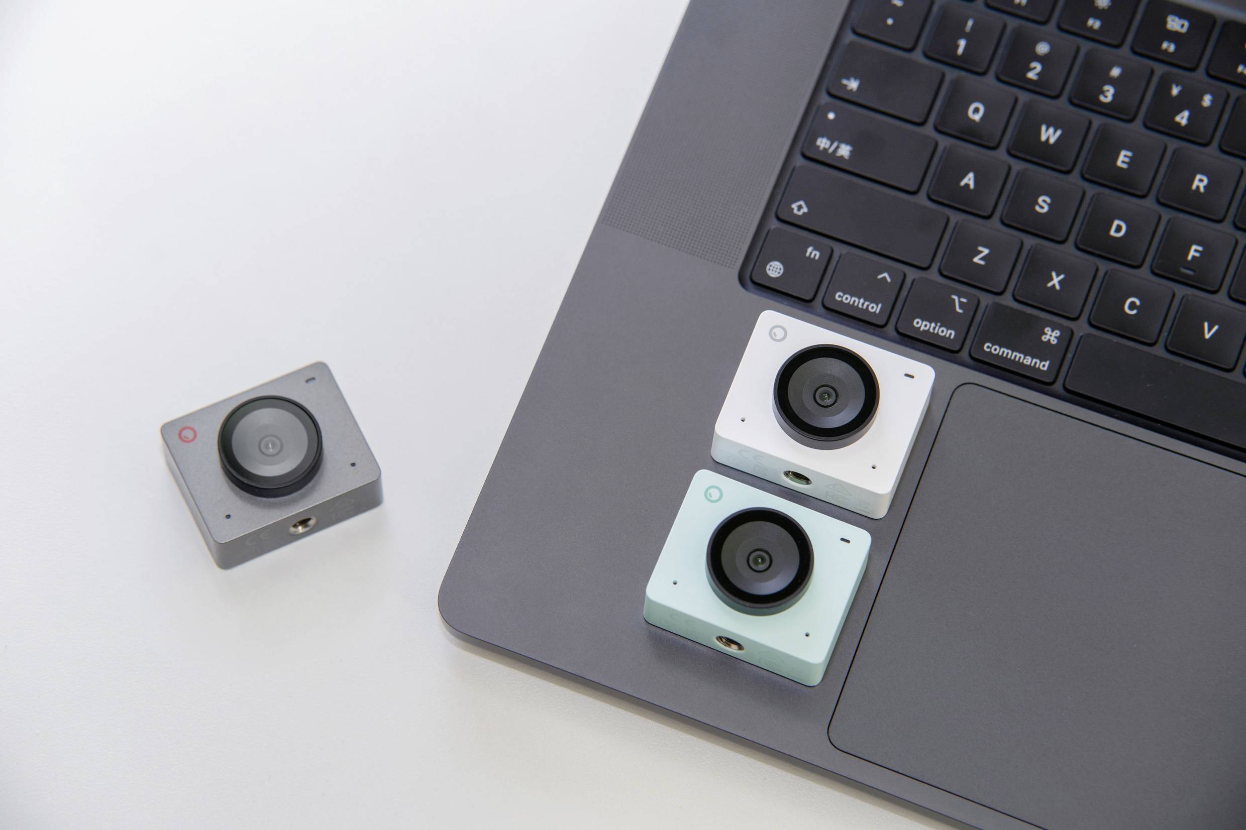 Three small cameras are lying next to and on a laptop on a table. Two cameras are positioned on the laptop.