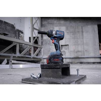 Cordless drill sits on a building site, surrounded by screws and metal parts. In the background are concrete walls and steel beams.