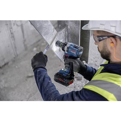A construction worker wearing a high-visibility safety vest is using an electric drill to work on metal. He is wearing a hard hat, gloves, and ear protection.