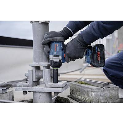 A worker is using a cordless power tool to tighten a metal connection on a construction site. He is wearing gloves.
