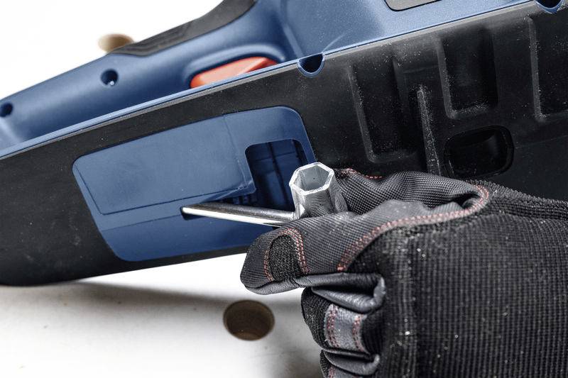 A gloved hand is using an Allen key to adjust a screw on a blue power tool.