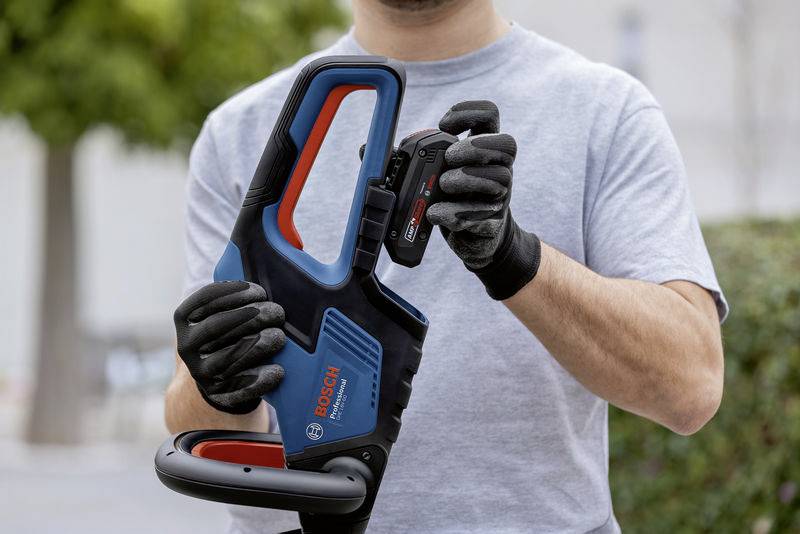 A man holding a blue electric tool with a red handle while inserting the battery. He is wearing black gloves.
