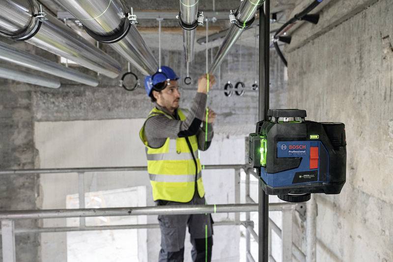 A construction worker wearing a hard hat and high-visibility vest is aligning levelling pipes using a Bosch laser in a building.