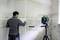 A man is levelling tiles with a green laser device on a tripod in a bathroom in need of renovation.