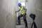 A construction worker in protective clothing is marking a line on a concrete wall using a laser level mounted on a tripod.
