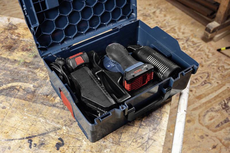 An open toolbox with a black electric jigsaw and accessories, positioned on a workbench.