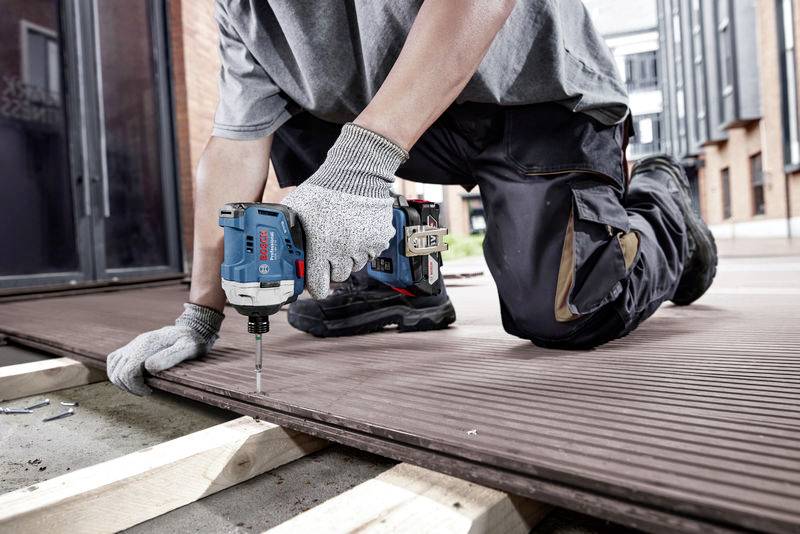 A person is kneeling and using a blue cordless drill to secure boards to a wooden frame outdoors.