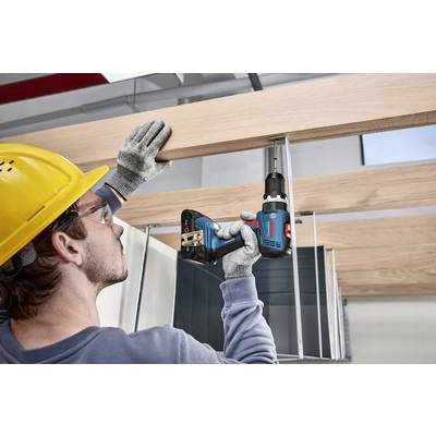 A worker wearing a hard hat and gloves is securing wooden battens to a metal structure using a cordless drill.