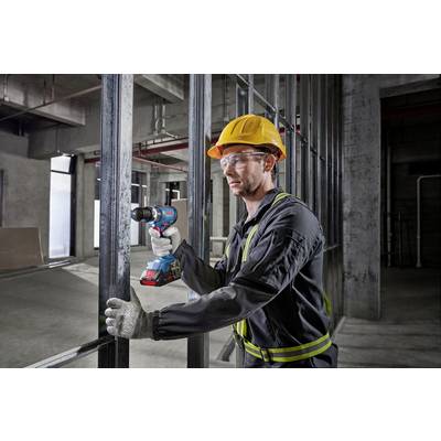A construction worker wearing a hard hat and gloves is using a drill to assemble metal frames in an unfinished building.