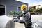 A worker in protective gear uses a power tool to cut metal in an industrial area with machinery in the background.
