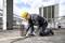 A construction worker in safety gear cuts metal rods with a power tool at a building site, with a partially constructed high-rise in the background.