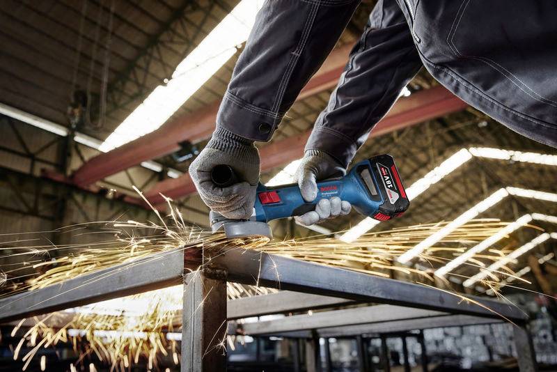 A person in workwear is using an angle grinder to cut metal. Sparks are flying away from the cutting point.