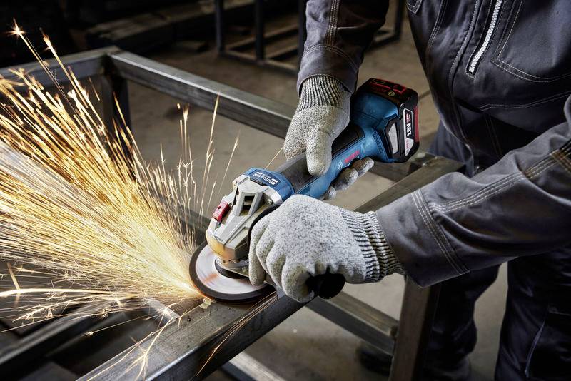 A person in work attire is using an angle grinder on a metal frame, with sparks flying.