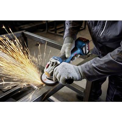 A person in work attire is using an angle grinder on a metal frame, with sparks flying.
