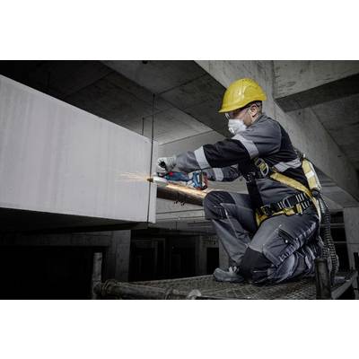 A worker wearing a hard hat and mask cuts a concrete structural beam with an angle grinder. Sparks fly as he cuts through the material.