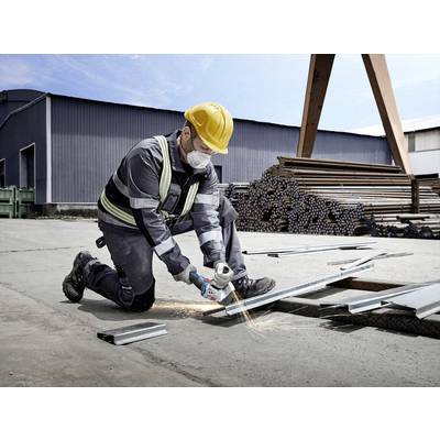 A worker is wearing protective clothing and using an angle grinder to cut metal. Warehouse buildings and pipes can be seen in the background.