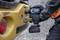 A person is using a Bosch cordless drill to tighten a large yellow metal nut on a construction vehicle.