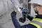 A construction worker in work attire and safety helmet is using a blue drill to work on a metal plate.