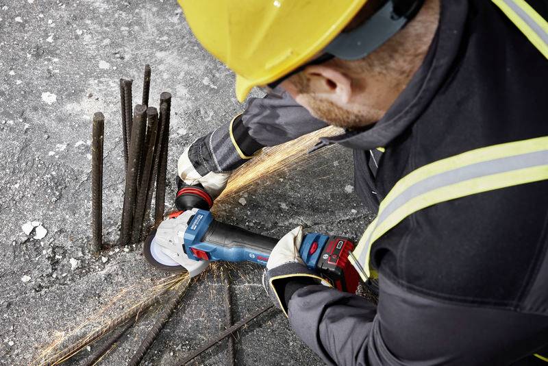 A construction worker wearing a hard hat grinds metal rods with an angle grinder, sparks flying. Workplace safety.