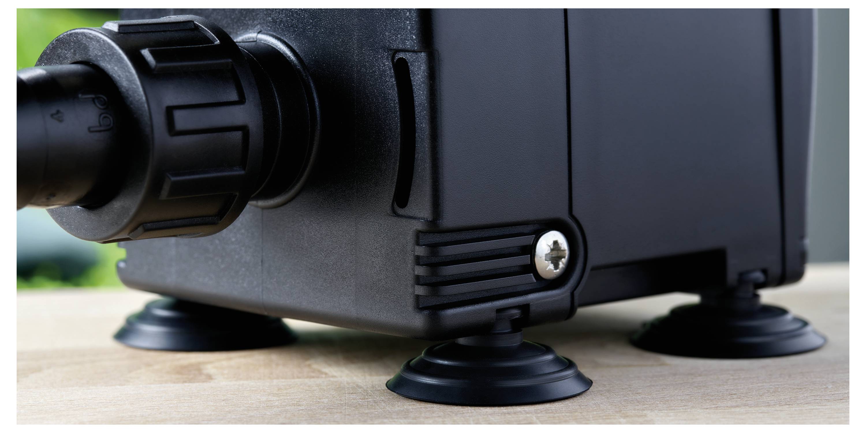 A close-up of a black pump with a hose connection and suction cup feet on a wooden surface, designed to reduce vibration.