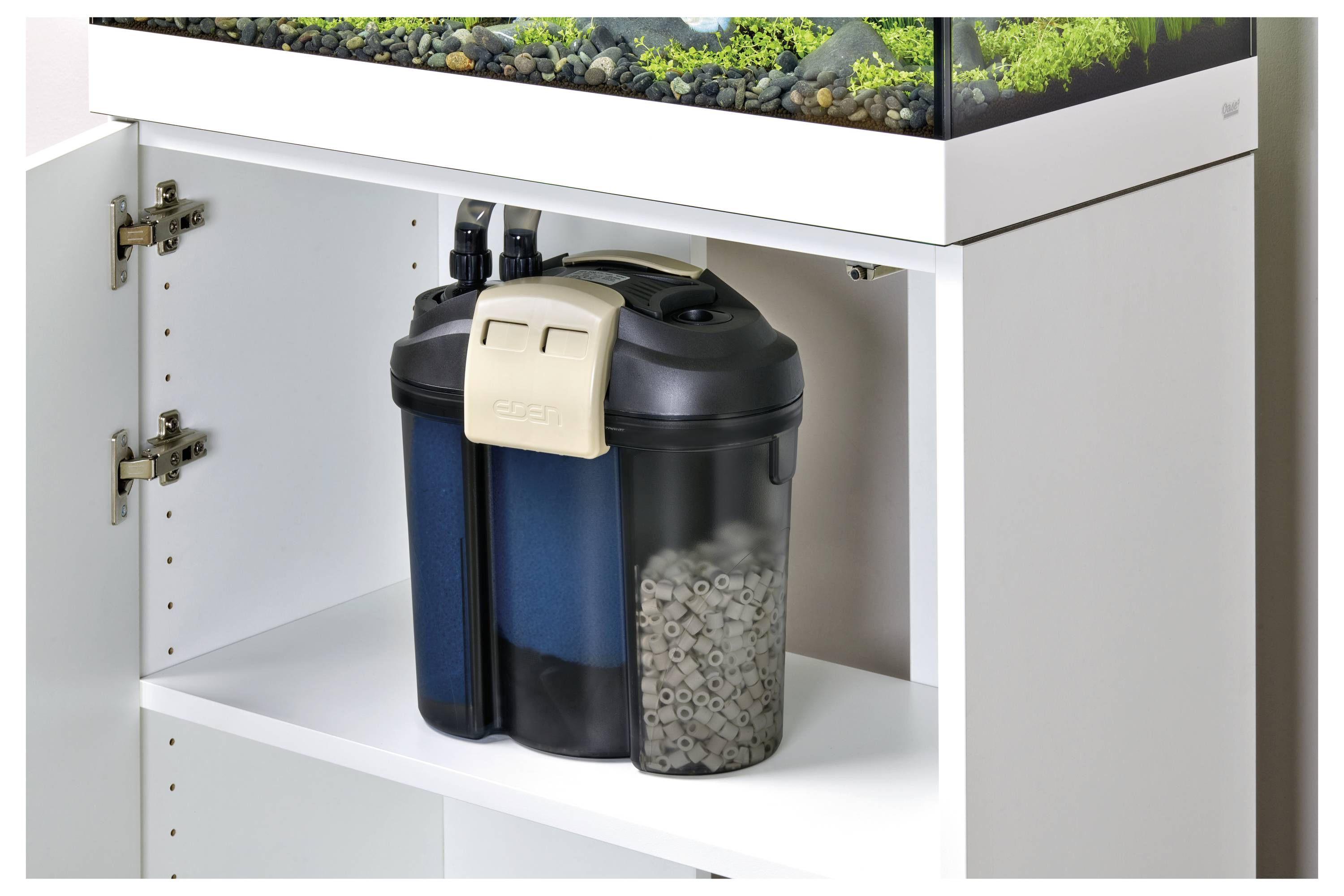 A canister filter under an aquarium cabinet with two chambers: one for blue filtration foam and another containing biological filter media.