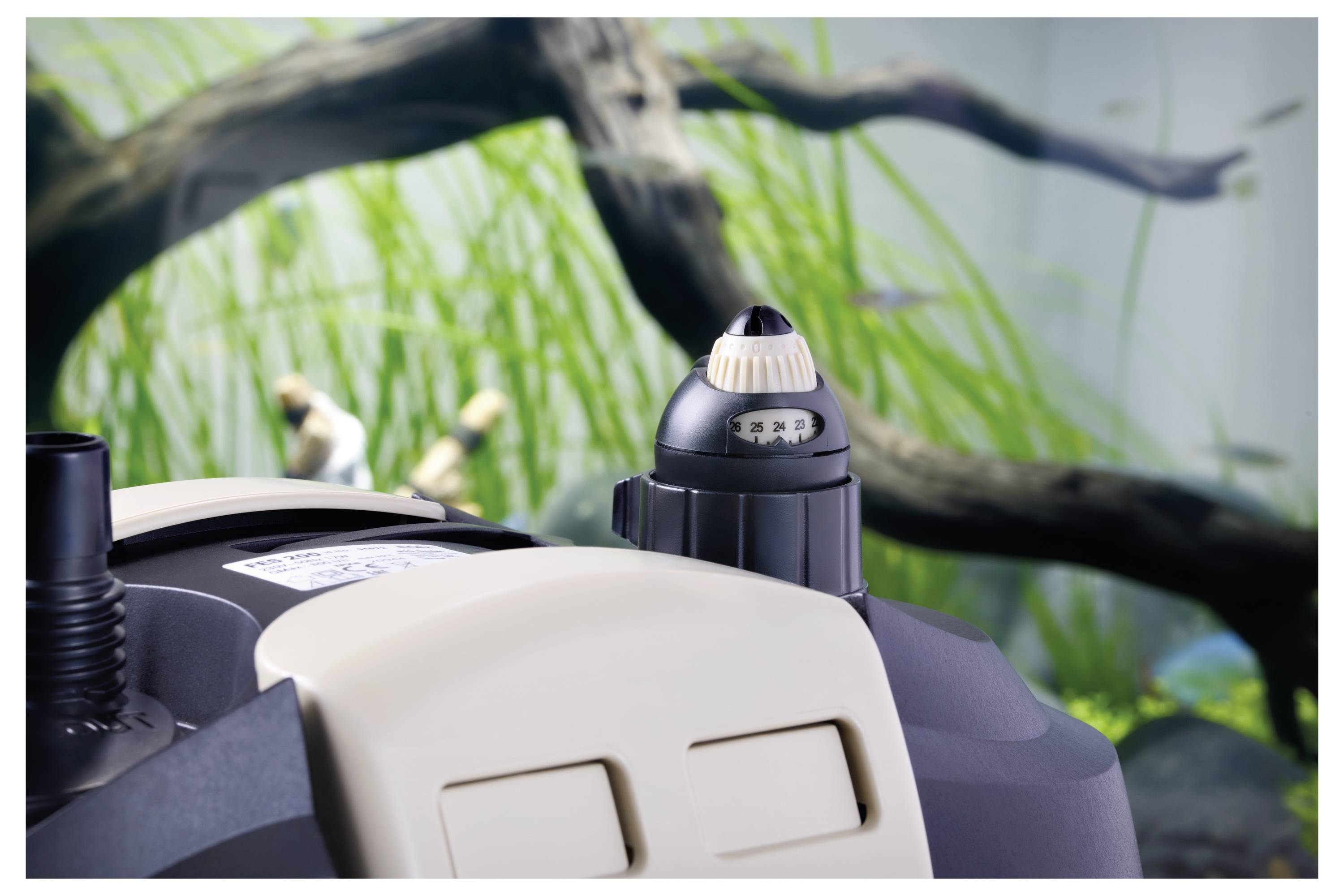 'Aquarium filter close-up with green plants and blurred branches in the background.'
