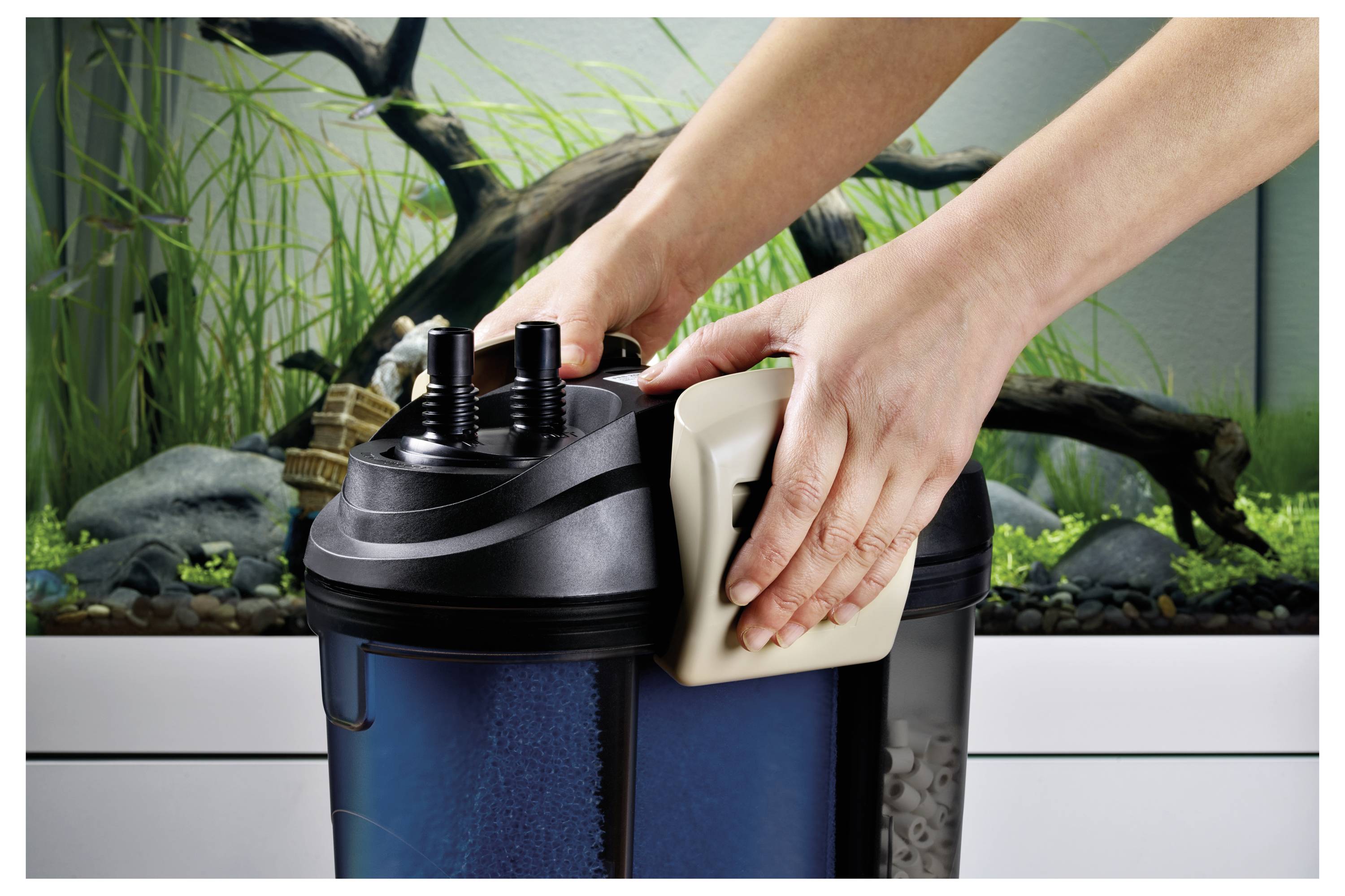 'Hands demonstrating the setup of an aquarium filter with clear water and aquatic plants in the background.'