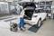 A person is vacuuming the boot of a white car in a garage. The boot is open, and a vacuum cleaner is being used.