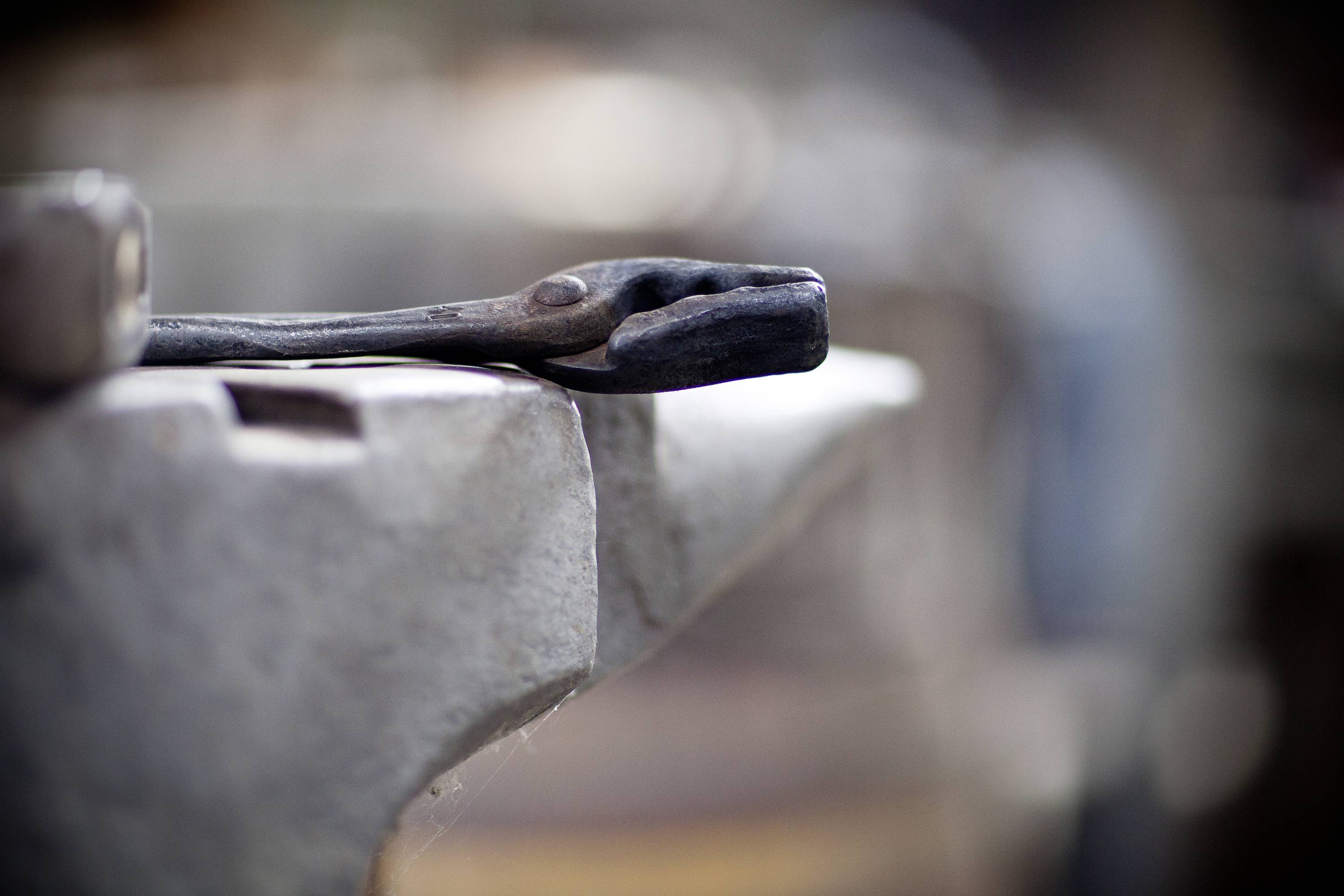 A pair of pliers lies on an anvil. The scene depicts a typical workshop environment.