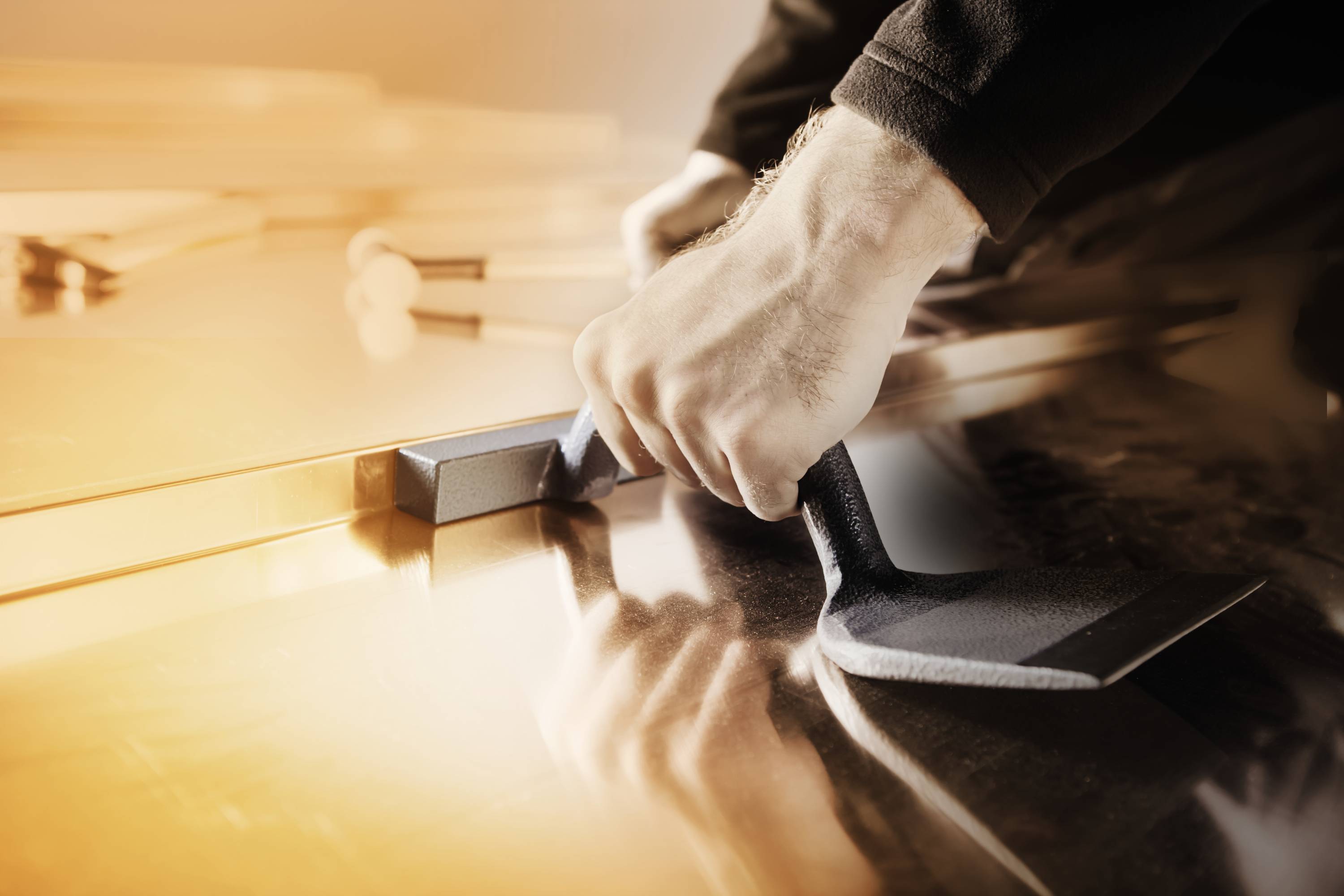 A person is using a hand tool to work on a metal piece in a workshop. Hands and tool are in focus.