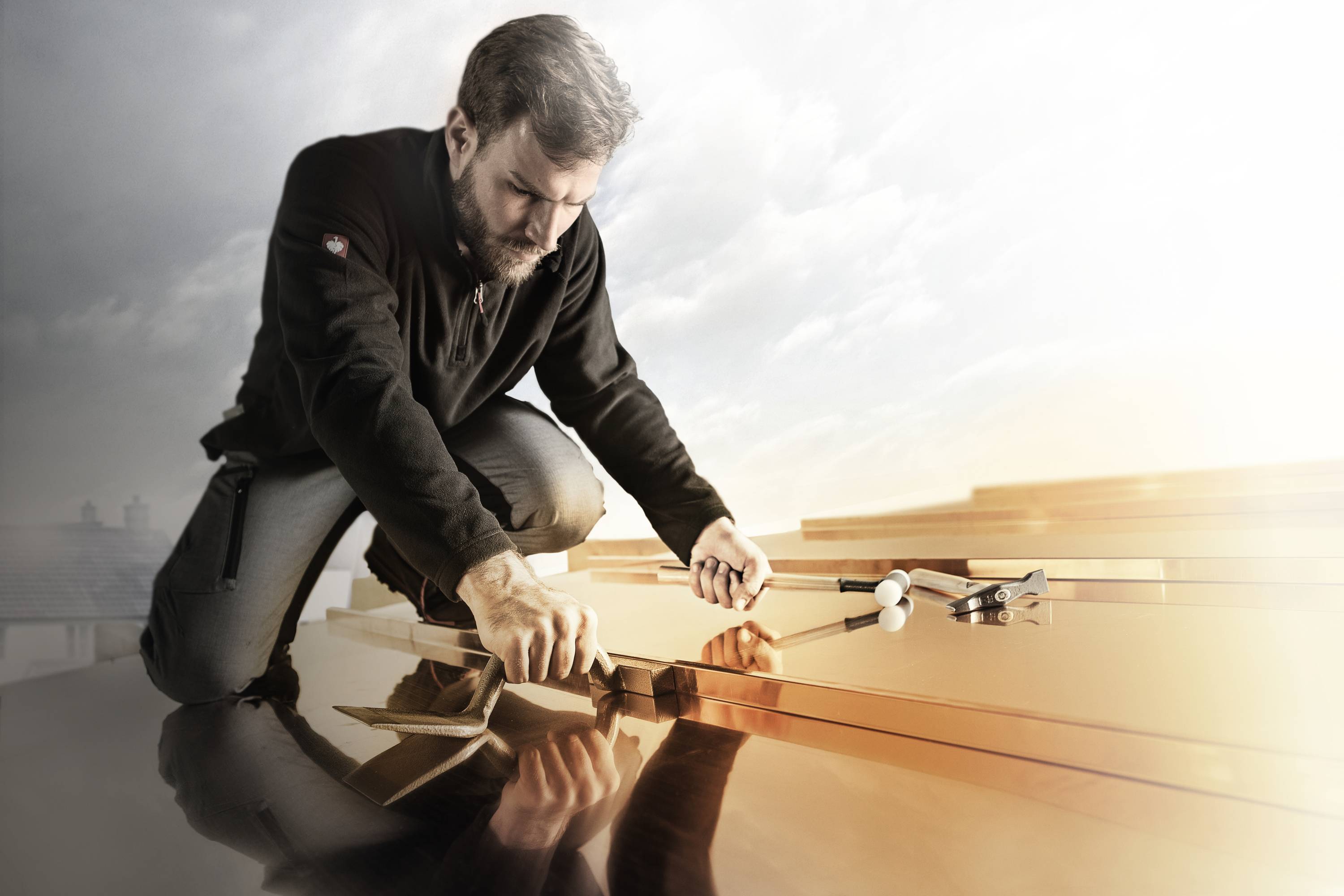 A man is working intently on a roof, using tools to secure metal sheets. The sky is visible in the background.