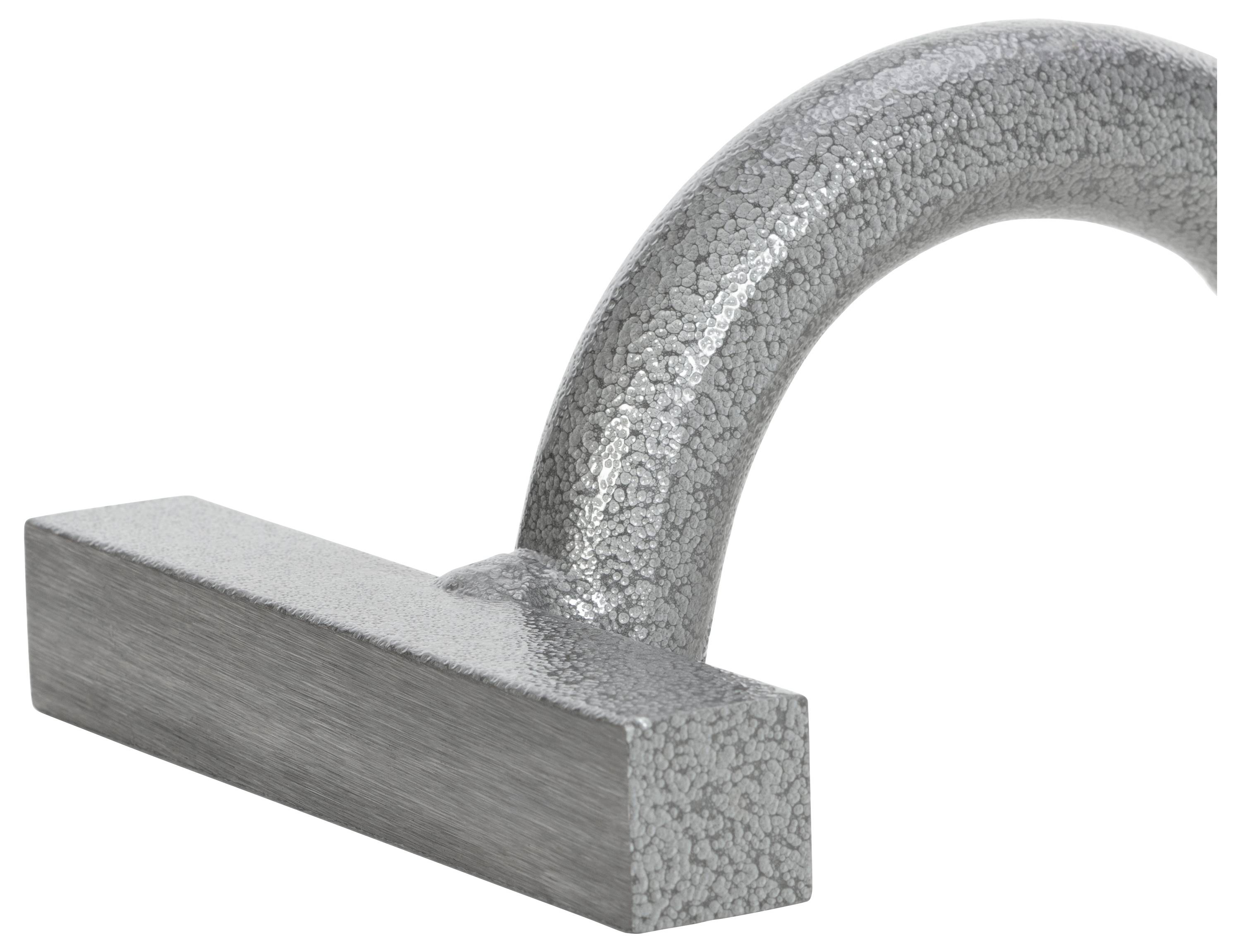 A curved grey metal handle lying on a white surface. The surface of the handle has a textured, grainy texture.