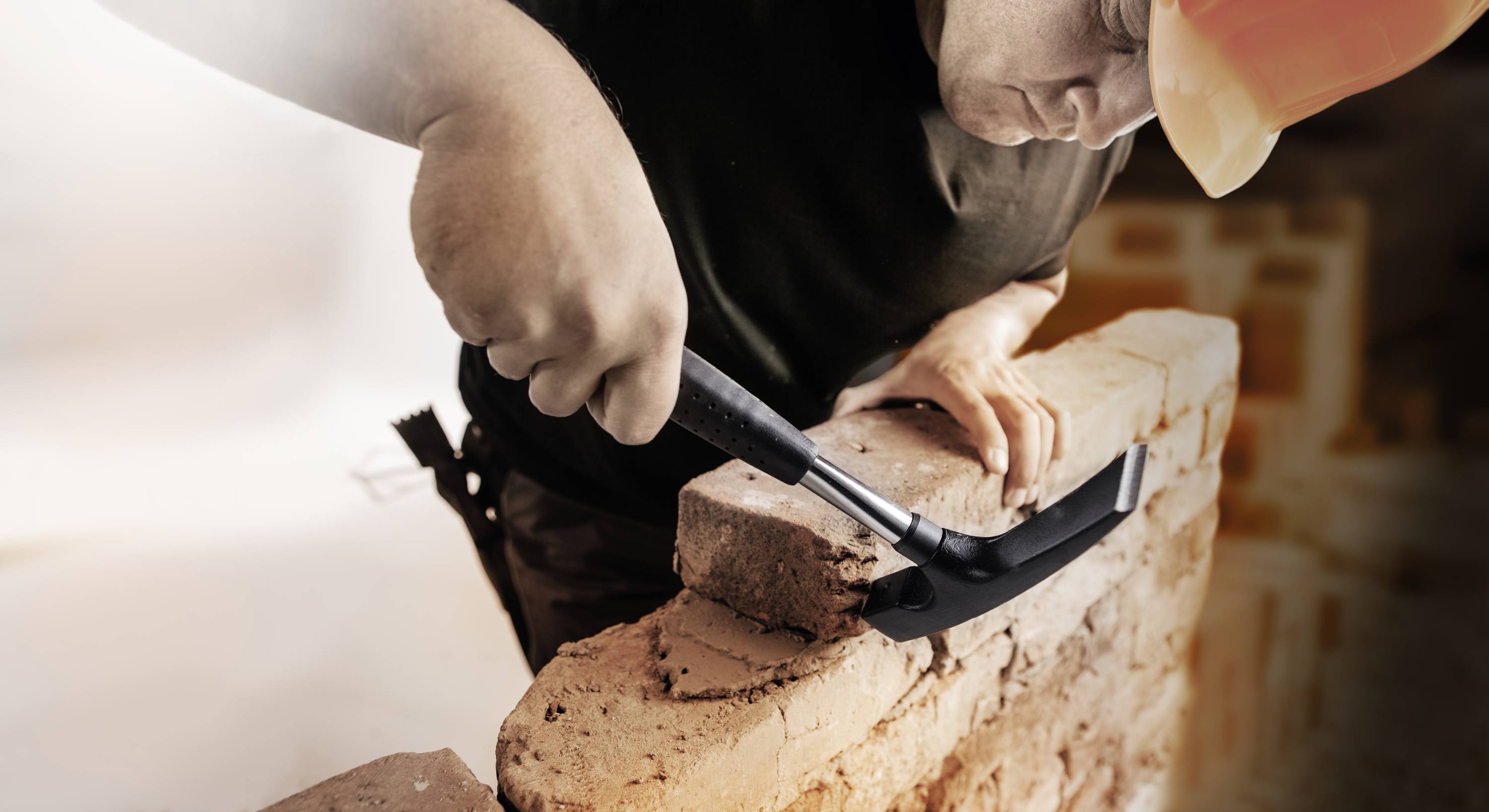 A construction worker is placing bricks in a wall while using a hammer.