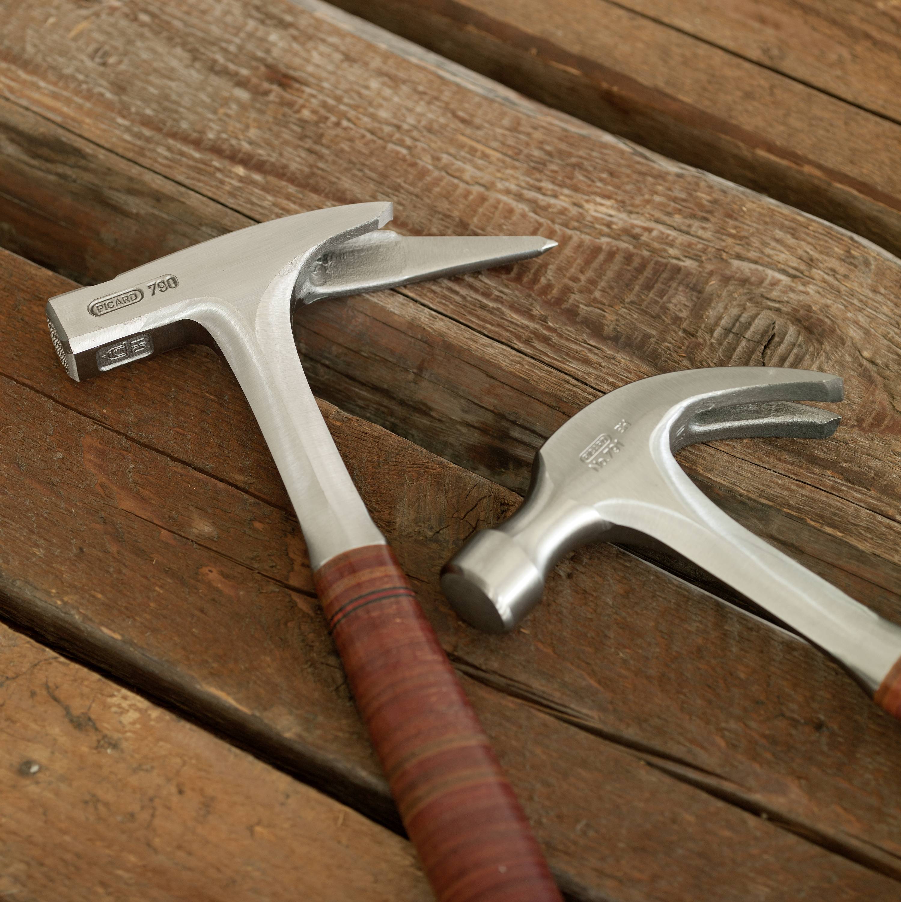 Two carpenter's hammers are lying on a wooden table. The front hammer has a leather-wrapped handle.