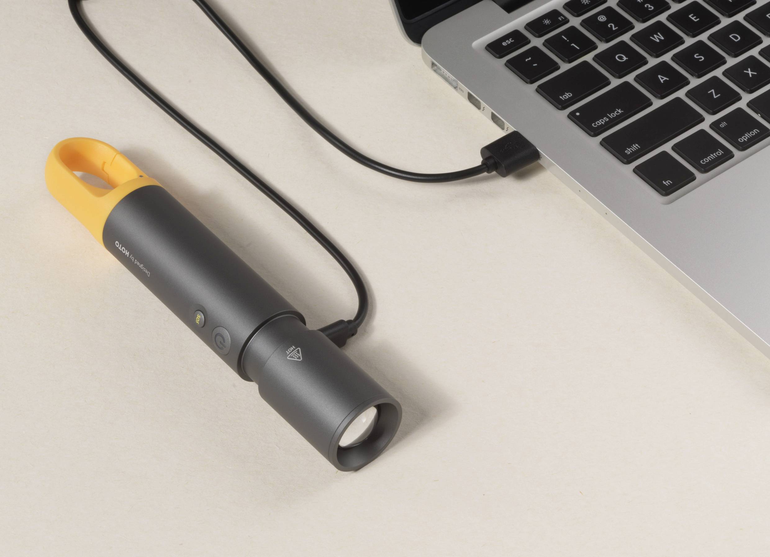 A black torch with an orange handle is connected to a laptop via a cable.<br><br>Note: In British English, "torch" is used instead of the American "flashlight", and the description follows a natural British phrasing.