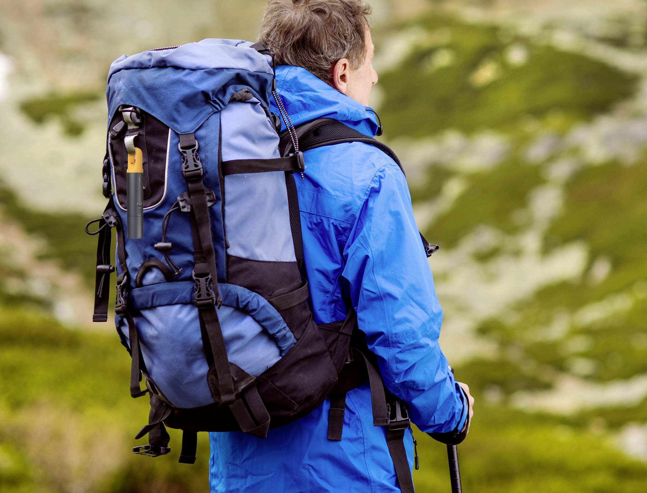 A person in blue outdoor clothing with a large rucksack gazes out over a mountainous landscape.