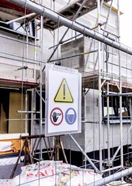 Construction site fence with a sign. Warning signs: Caution Danger, Stop Signal, Hard Hat Required. Buildings in the background.