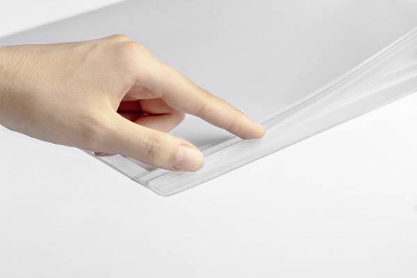 A finger gently lifts a transparent plastic film that is resting on a smooth, white surface.