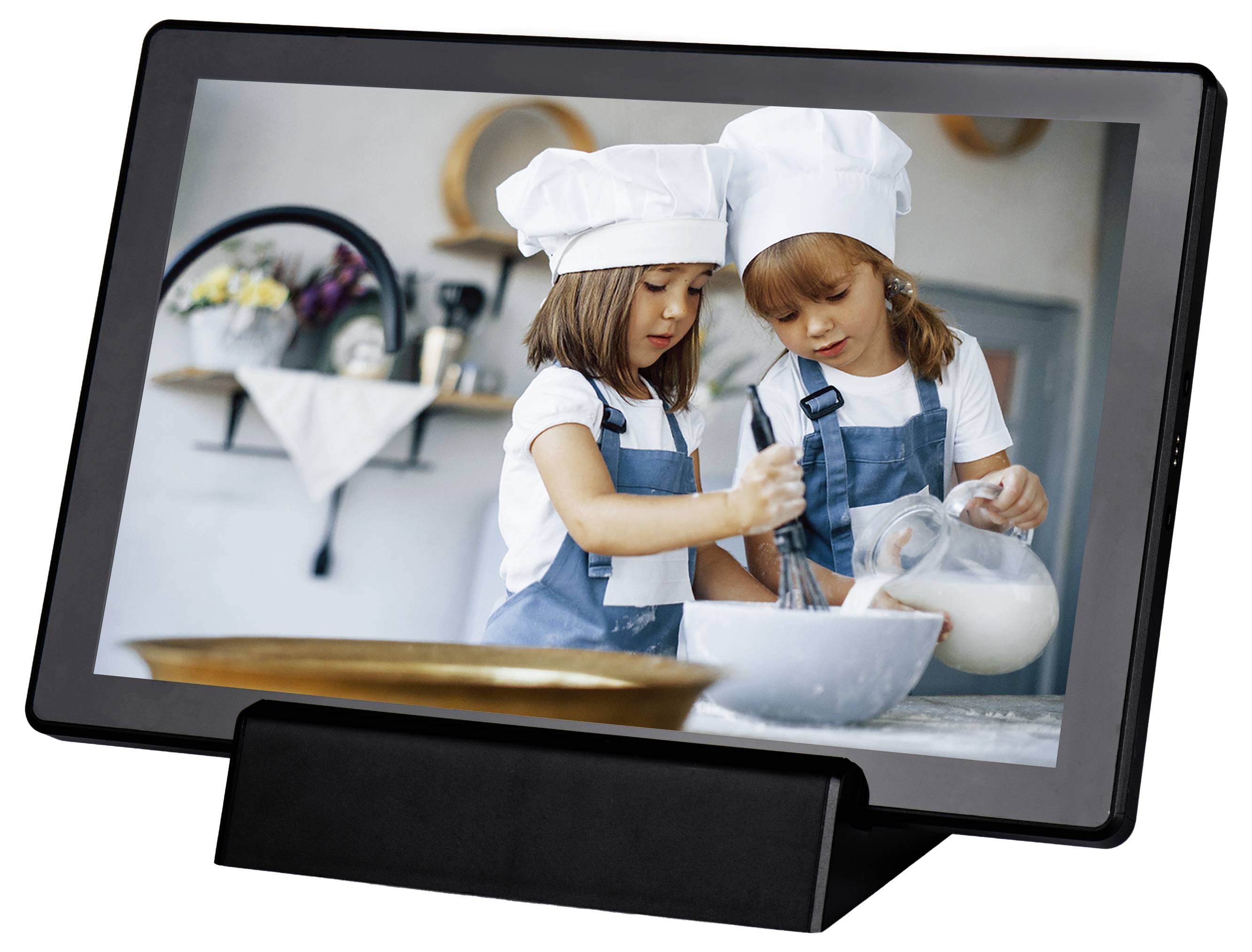 Two children in chef's hats and aprons are stirring dough in a bowl while standing in a kitchen. One child is holding a measuring jug.
